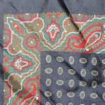 Dark blue background silk pocket square with a red green and white paisley border and a small central design